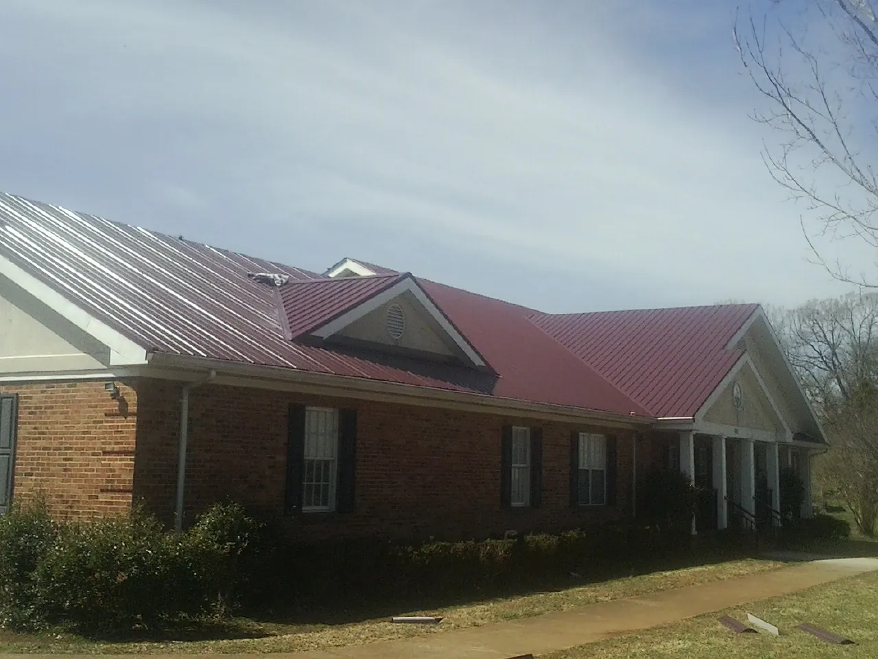 Red metal roof with gabled entries on a long brick building, from a Hail Damage Roof Repair job in Scotland Neck