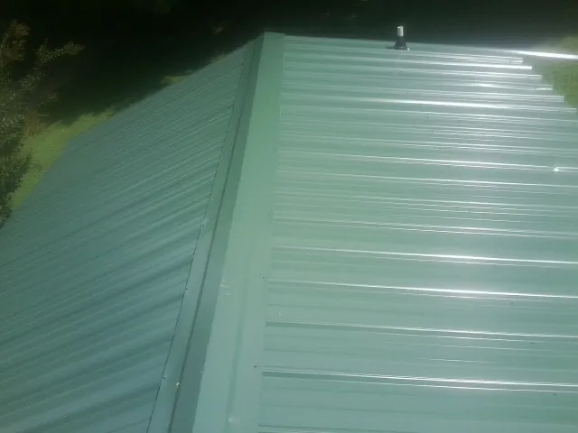 New green metal panels meeting at the ridge of a roof — Flat Roof Repair work by our crew in Scotland Neck
