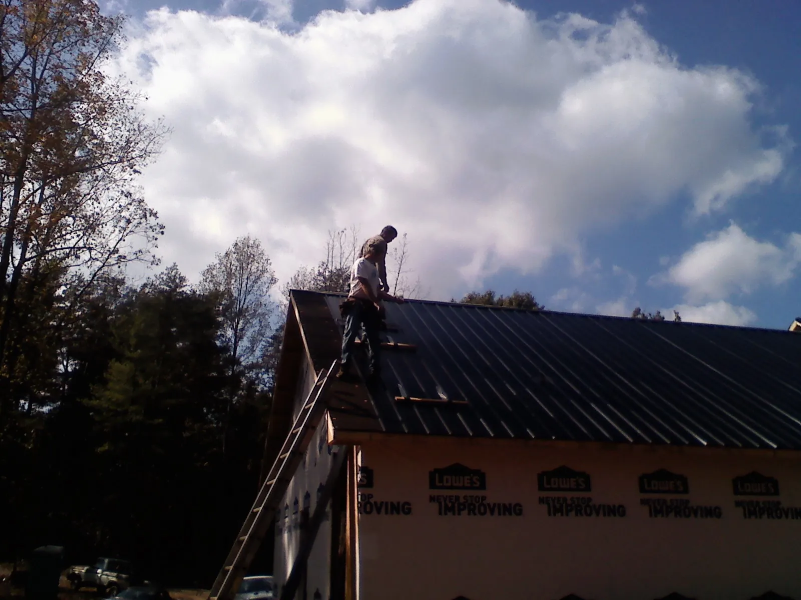 Roofer fastening dark metal panels high against a cloudy sky, from a Roof Inspection job in Scotland Neck