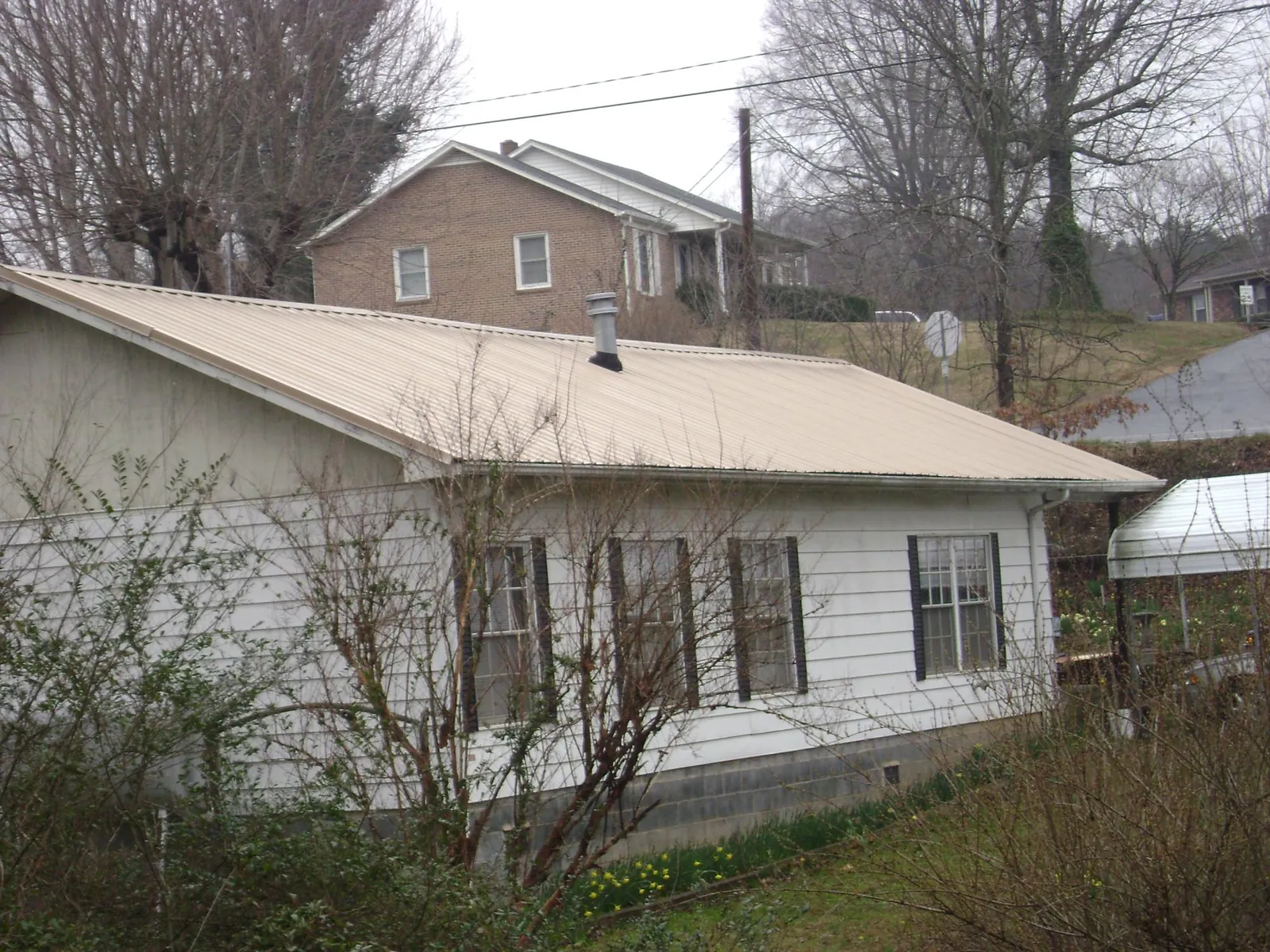 Tan metal roof on a white sided house set into a hillside — Commercial Roofing by Roofing Brothers in Scotland Neck