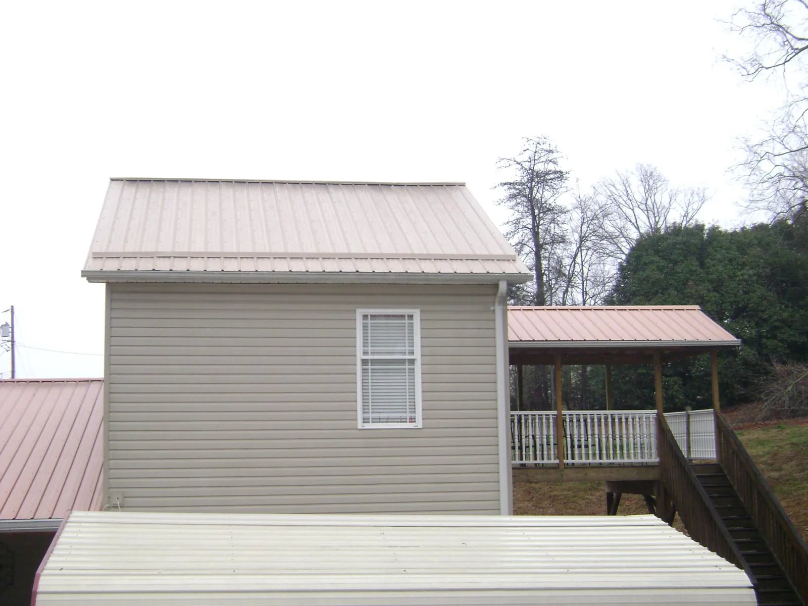 Tan metal roofs on a two story addition and attached porch, from a Roof Replacement job in Scotland Neck